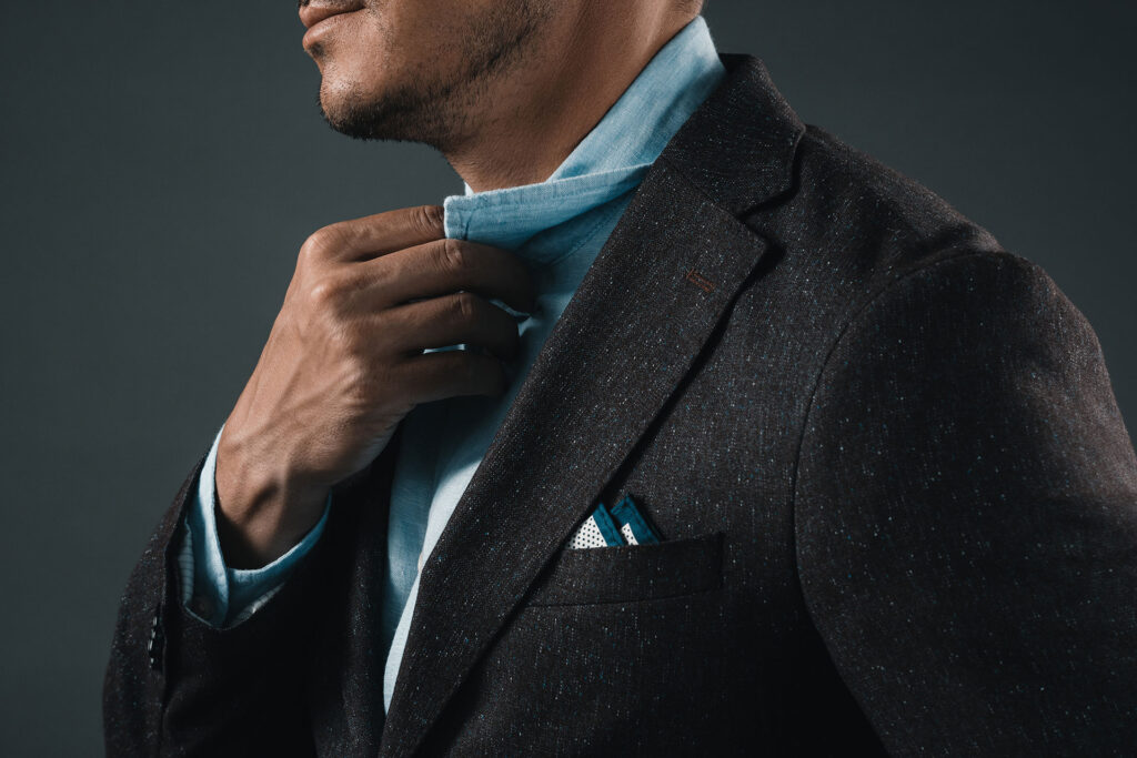 Mężczyzna poprawiający jasnoniebieski kołnierz pod marynarką w ciemnym kolorze z poszetką.