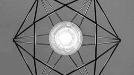 Geometryczna lampa z metalowymi prętami i jasną żarówką w środku na szarym tle